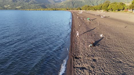 Flying-over-the-shores-of-Lake-Villarrica,-people-on-the-beaches,-near-Araucania-in-Chile