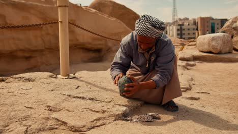 Egyptian-archaeologist-hitting-the-granite-surface-with-volcanic-stone-at-unfinished-obelisk-historical-site-in-stone-quarries-of-ancient-Egypt-in-Aswan