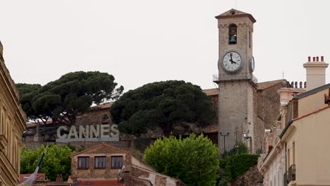 Clock-tower-and-Cannes-sign-by-lush-trees-and-historic-buildings-in-France