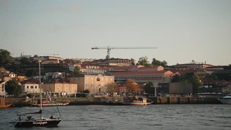 Scenic-Porto-riverside-with-sailboat,-historic-buildings,-and-construction-crane-at-sunset