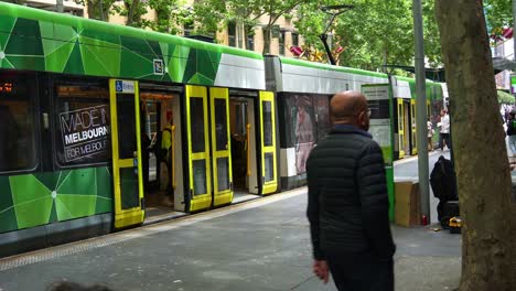 Passengers-disembark-the-tram-at-the-Swanston-Street-and-Bourke-Street-tram-stop,-and-then-the-tram-slowly-departs-the-stop-in-Melbourne-city