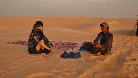 Hombre-Y-Mujer-Sentados-En-Una-Manta-Junto-A-Una-Fogata-En-El-Desierto-Al-Atardecer