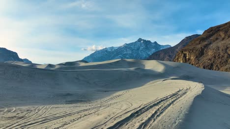 Person-walking-across-Sarfaranga-Cold-Desert-dunes-with-mountain-backdrop-in-Skardu-Valley---aerial