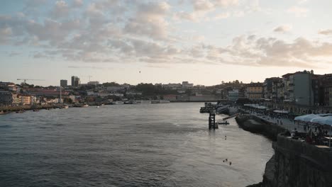 Blick-Auf-Das-Flussufer-Von-Porto-Durch-Die-Brückengeländer-Dom-Luís-I-Bei-Sonnenuntergang,-Mit-Gebäuden-Am-Wasser-Und-Einem-Ruhigen-Fluss