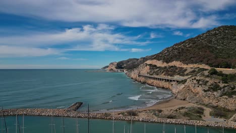 Vista-Panorámica-De-La-Costa-Y-El-Puerto-De-Ginesta-Con-Acantilados-Escarpados-Y-Tranquilas-Aguas-Azules.