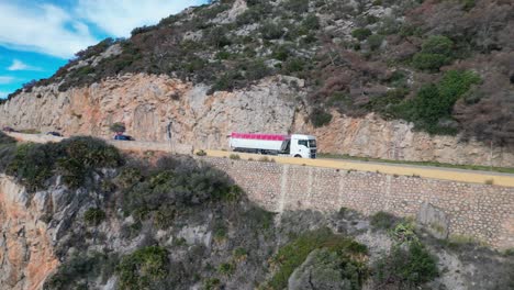 Truck-driving-a-scenic-coastal-road-along-rocky-cliffs-overlooking-the-ocean-in-Port-of-Ginesta,-Barcelona