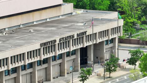 United-States-Mint-aerial-shot-with-prominent-signage,-American-flag,-and-people-near-the-entrance