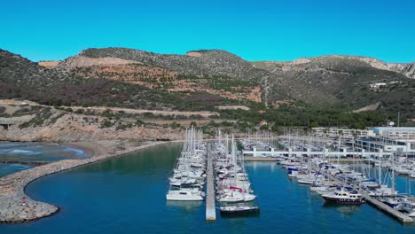 Marina-with-yachts-docked-at-Port-Ginesta-in-Barcelona-on-a-clear,-sunny-day,-aerial-view