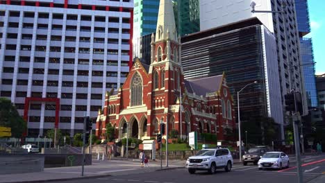 Tilt-up-street-shot-capturing-the-heritage-listed-Victorian-Gothic-Revival-architecture,-Albert-street-uniting-church-against-corporate-office-blocks-with-traffics-on-the-foreground