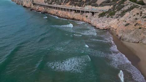 Coast-and-port-of-ginesta-in-barcelona-with-waves-crashing-on-the-rocky-shore,-aerial-view