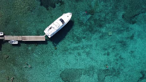 Nautical-Tourism,-Yacht-moored-to-wooden-Jetty-in-clear-blue-Lagoon,-Drone-top-down