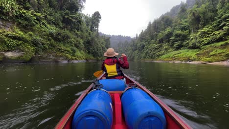 Mujer-Con-Chaqueta-Roja,-Sombrero-Y-Chaleco-Salvavidas-Amarillo-Rema-Rápidamente-Por-El-Río-Whanganui-En-Su-Canoa-Entre-Dos-Acantilados-Del-Bosque