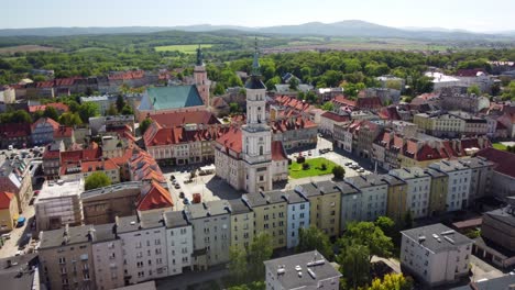Aerial-footage-of-Prudnik,-capturing-the-historic-town-center-with-its-distinctive-church,-town-hall,-and-charming-red-tiled-roofs