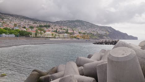 Wave-breakers-near-Atlantic-ocean-shore-with-city-in-background,-Madeira