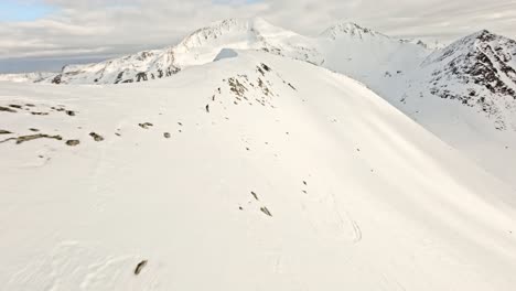 People-skiing-down-snowy-Norway-mountains,-aerial-FPV-view