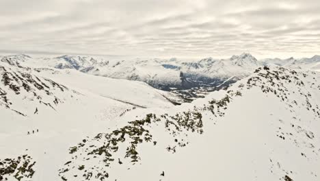 Gruppe-Von-Menschen-Am-Rande-Eines-Riesigen-Schneebedeckten-Berges,-Bereit-Zum-Skifahren,-Luftaufnahme