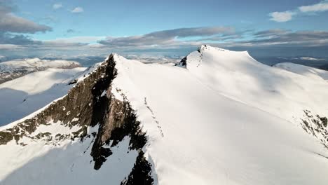 Long-line-of-people-walking-up-to-summit-mountain-peak-for-skiing,-aerial-view