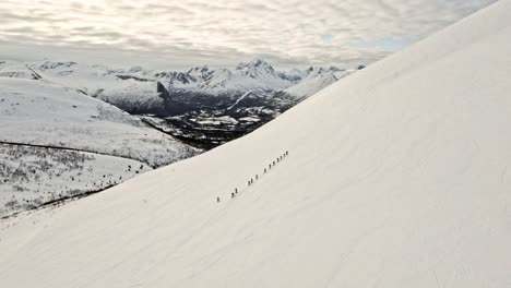 Group-of-people-hiking-on-white-snowy-mountain,-aerial-view