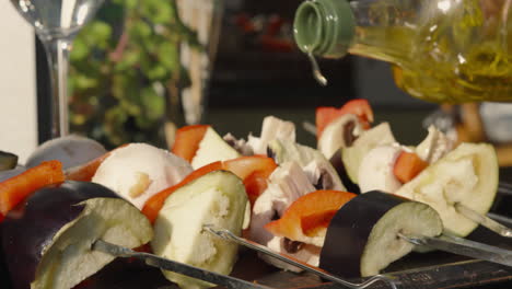 Olive-Oil-Drizzled-on-Shish-Vegetable-Kebabs-Ready-for-BBQ-with-Mushrooms,-Aubergine,-Peppers-and-Wine-Glass-in-Background---Slow-Motion