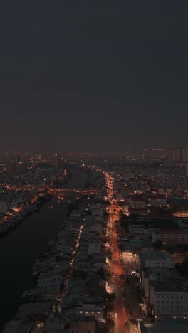 Waterfront-view-of-urban-Saigon-canal-in-Ho-Chi-Minh-City-at-night-featuring-shanty-houses-and-road-with-traffict