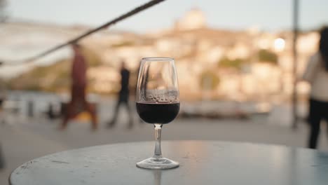 glass-of-red-port-wine-on-a-café-table-with-blurred-Porto,-Portugal-background