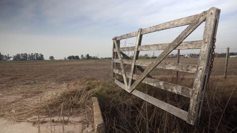 Weite-Sicht-Auf-Ein-Altes-Holztor-In-Einem-Feld,-Das-Im-Wind-Schwingt