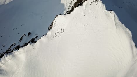 Group-of-people-preparing-to-ski-from-peak-of-snowy-mountain-in-Norway,-aerial-top-down-view