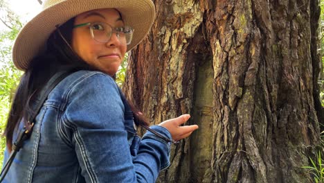 An-Asian-woman-in-a-denim-jacket-and-hat-knocks-on-a-hidden-door-she-found-in-a-tree-in-the-forest