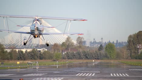 Doppeldecker-Stuntflugzeug-Landet-Auf-Landebahn,-Brücke-Im-Hintergrund,-Zeitlupe-Von-Hinten