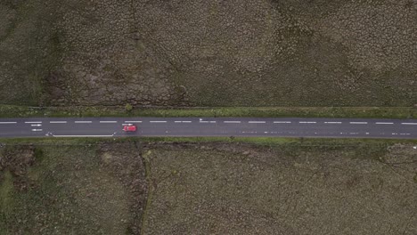 Lone-red-car-drives-narrow-road-through-rugged-Scottish-moor-land