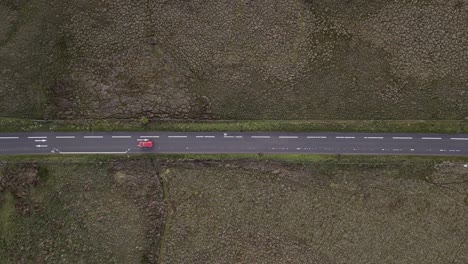 Einsames-Rotes-Auto-Fährt-Auf-Schmaler-Straße-Durch-Zerklüftetes-Schottisches-Moorland