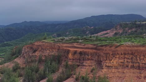 Wide-aerial-panning-shot-of-red-sandy-cliffs-on-the-island-of-Maui-with-dark-clouds-in-the-background