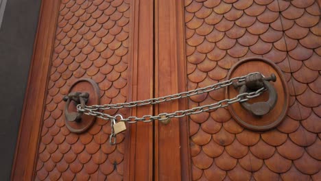 Ornate-wooden-Roman-door,-with-chain-through-door-knockers