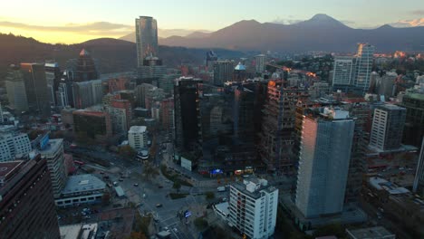 Aerial-drone-reveals-MUT-urban-market-at-Santiago-de-Chile-city-sunset-mountain-skyline-of-El-Golf-neighborhood-with-Andean-Cordillera-background