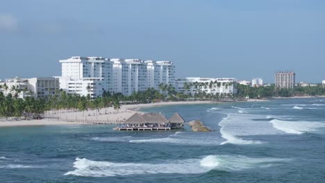 Teleaufnahme-Der-Luftaufnahme-Von-Meereswellen,-Die-Auf-Den-Weißen-Sand-Von-Playa-Hemingway-Krachen,-Mit-Hotel-Dahinter