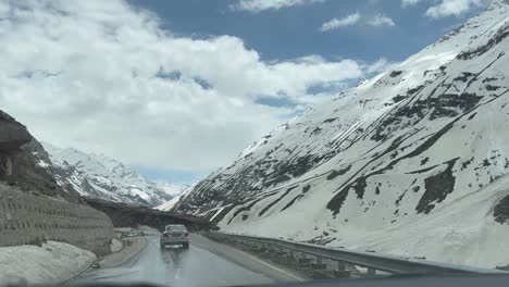 Das-Auto-Fährt-über-Eine-Straße,-Auf-Der-Viele-Schneebedeckte-Berge-Sichtbar-Sind-Und-Eine-Kleine-Straße