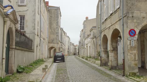 Pan-shot-of-quaint-street-with-historic-buildings-on-both-sides-of-an-empty-road-in-La-Rochelle,-France-on-a-cloudy-day