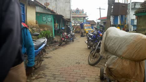 South-Indian-rural-village-street-with-motorcycles-parked-outside-homes,-Indian-men-in-traditional-wear-lungi