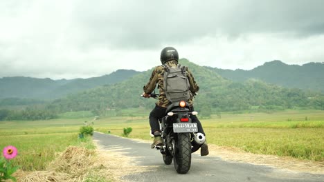 Biker-guy-driving-a-motorbike-in-a-rice-field-area-with-mountain-views