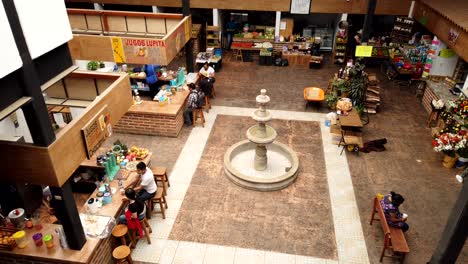 Timelapse-A-Vista-De-Pájaro-De-Gente-Comprando-Y-Comiendo-En-El-Mercado-Local-De-Tapalpa,-Con-Una-Fuente-Central.