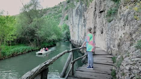 Woman-on-eco-trail-escarpment-boardwalk-watches-pedalos-pass-on-river