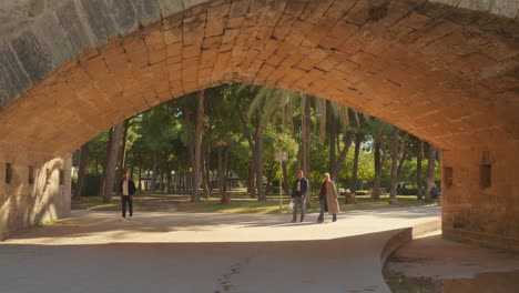 Tilt-down-shot-of-local-people-walking-under-the-Puente-del-mar-bridge-at-the-Turia-Gardens-in-Valencia,-Spain-at-daytime
