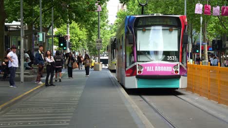 El-Tranvía-Llegó-A-La-Parada-Frente-A-La-Biblioteca-Estatal-De-Victoria,-Con-Pasajeros-Esperando-Para-Abordar,-Ciclistas-Y-Repartidores-Recorriendo-El-Carril,-El-Vibrante-Estilo-De-Vida-Urbano-De-Melbourne.