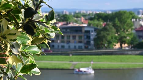 Boat-going-along-the-Vistula-River-below-Wawel-Castle,-Kraków,-Poland