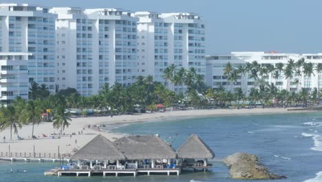 Breakwater-protects-scenic-covered-eating-area-and-beach-of-white-hotels,-aerial