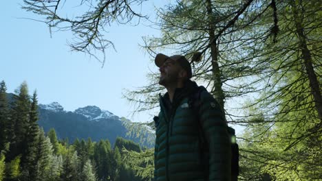 Enthusiastic-young-hiker-with-day-pack-looks-around-at-forest-and-mountain-scenery