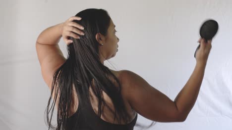 Hispanic-adult-woman-with-her-back-to-the-camera-combs-her-long-black-hair-with-a-comb-after-bathing