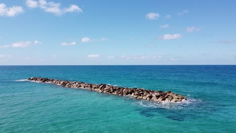 Crystal-clear-waters-and-blue-skies-over-Venus-Beach-in-Cyprus,-with-gentle-waves-breaking-against-a-rocky-breakwater