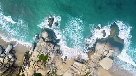 Vista-De-Drones-Desde-Arriba-Olas-De-Agua-Azul-Y-Blanca-Chocan-Con-Una-Gran-Roca-En-El-Mar-De-Santa-Marta,-Columbia