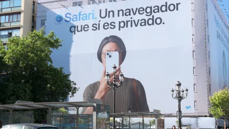 In-downtown-Madrid,-people-walk-past-a-prominent-billboard-by-Apple,-the-American-multinational-technology-company